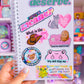 Notebook with colorful stickers held in front of a shelf with toys and stationery items.